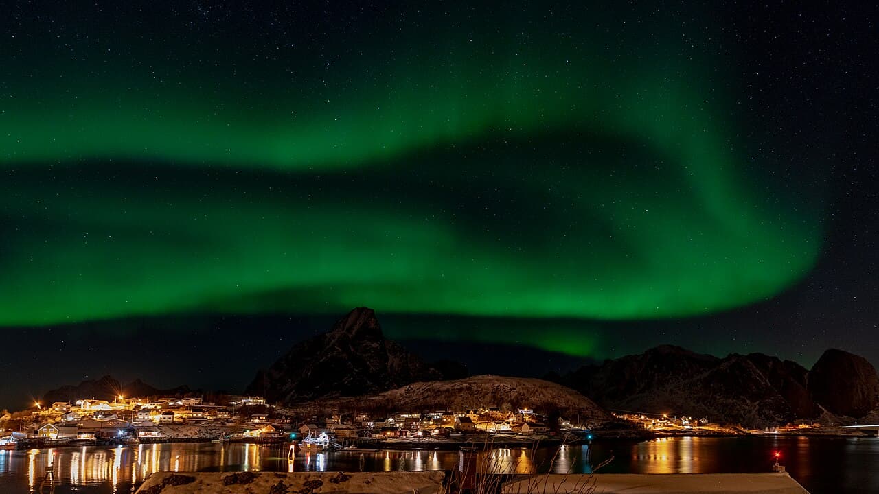 The northern lights glowing over a lit fishing village in the Lofoten Islands