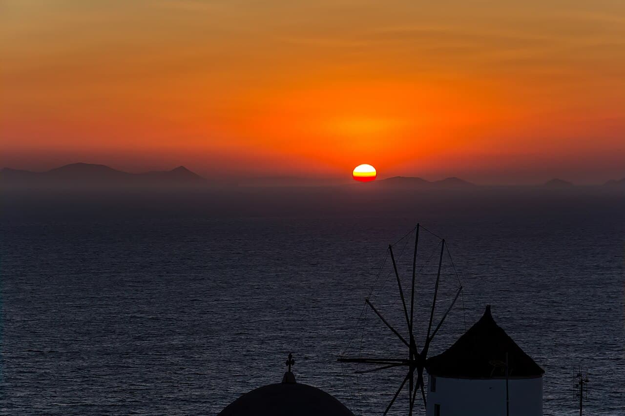 Sunset over the Aegean behind a whitewashed Santorini windmill